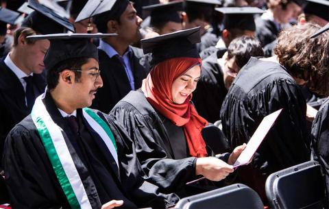 Graduates look at their diplomas while seated in the audience
